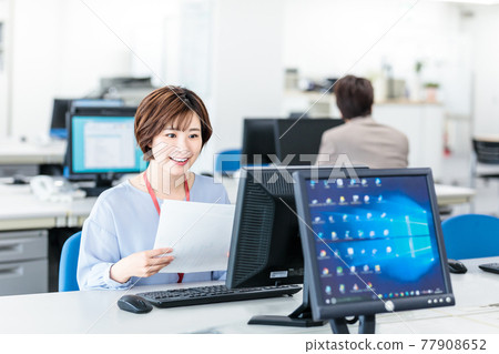 使用計算機的一個年輕女商人在一個明亮的辦公室 使用計算機的一個年輕女商人在一個明亮的辦公室 77908652