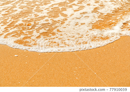 A sea wave with white foam splashes out onto the yellow sandy shore A sea wave with white foam splashes out onto the yellow sandy shore 77910039