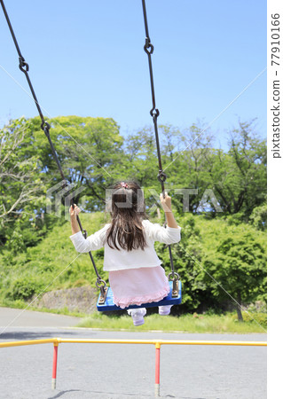 A female elementary school student in the back (6 years old) playing on a swing 77910166