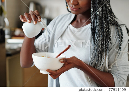 Woman pouring milk in granola bowl 77911409