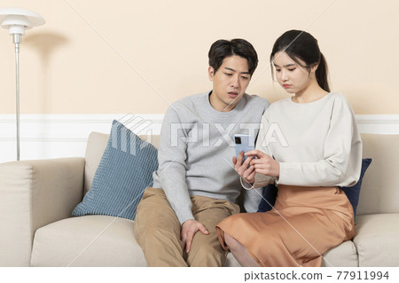 disappointed Asian married couple using smartphone on sofa at home 77911994