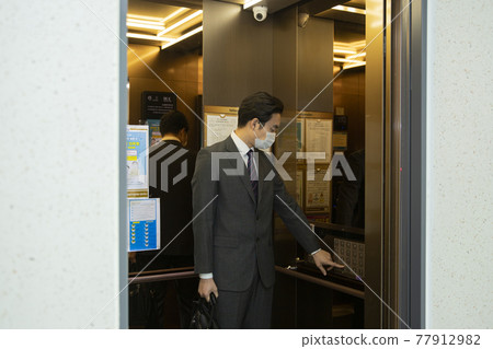 Asian business man in suit wearing mask in elevator 77912982
