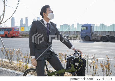 Asian man in smart casual suit wearing mask on bicycle, on the way to work Asian man in smart casual suit wearing mask on bicycle, on the way to work 77912993
