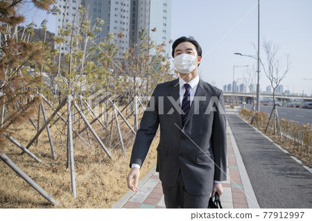 Asian business man in suit wearing mask on way to work by foot Asian business man in suit wearing mask on way to work by foot 77912997