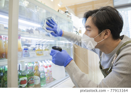 Asian man with mask sanitizing store during covid Asian man with mask sanitizing store during covid 77913164