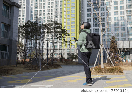 Asian delivery male courier with thermal bag, delivering order on foot, checking location using phone Asian delivery male courier with thermal bag, delivering order on foot, checking location using phone 77913304