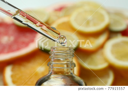 Pipette with oil over the bottle against different citrus slices 77915557