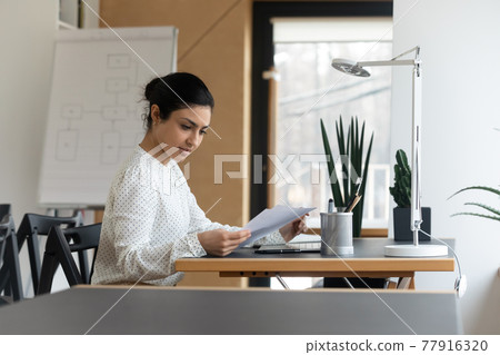 Focused Indian businesswoman using laptop, reading checking financial documents Focused Indian businesswoman using laptop, reading checking financial documents 77916320