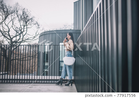 Woman in jeans and beige blouse walking and talking on the phone Woman in jeans and beige blouse walking and talking on the phone 77917556