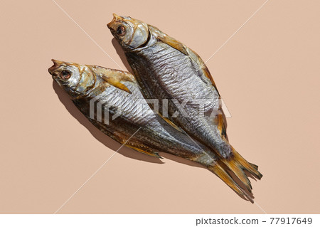 Two dried or jerky salty taranka, yummy clipfish on pink background. Popular beer appetizer. Traditional way of preserving fish. Close up 77917649