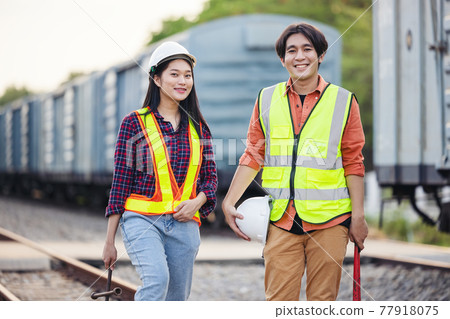 Maintenance technician in a safety suit stands beside a freight train with the wrench. Asian workers work within the rail transport industry. Engineer and repair concept. Safety first Maintenance technician in a safety suit stands beside a freight train with the wrench. Asian workers work within the rail transport industry. Engineer and repair concept. Safety first 77918075