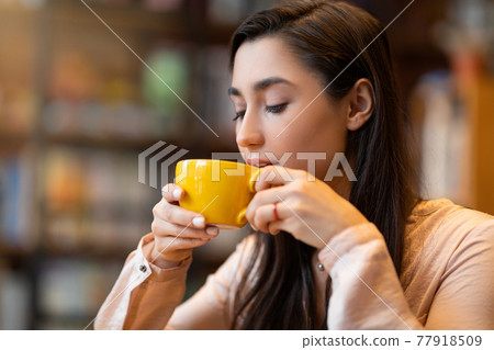 Time for coffee. Carefree arab lady sitting at cafe, holding mug of hot drink and enjoying aroma of coffee 77918509