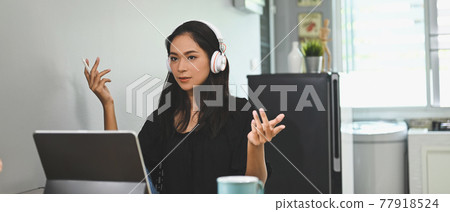 A beautiful woman is using a computer tablet and making a video conference at the wooden working desk. 77918524