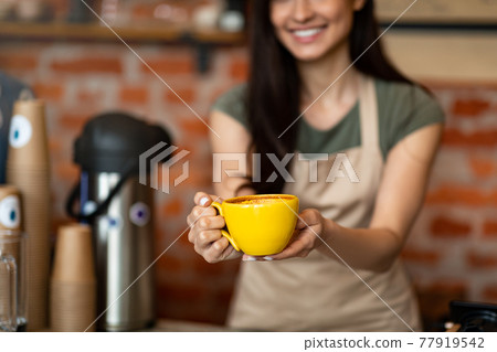 Unrecognizable female barista welcoming guests at coffee house counter, offering cup of hot beverage, closeup, crop Unrecognizable female barista welcoming guests at coffee house counter, offering cup of hot beverage, closeup, crop 77919542