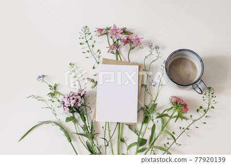 Summer greeting card, invitation mockup. Garden and wild meadow flowers. Floral banner and cup of coffee. Shepherd's purse, dianthus and aquilegia plants isolated on white table background. Flat lay. 77920139