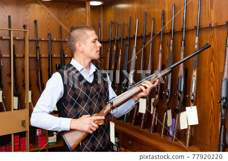Interested man choosing hunting rifle in gun shop 77920220