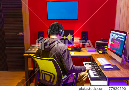 male asian music producer arranging a song on midi keyboard and computer in home recording studio 77920290