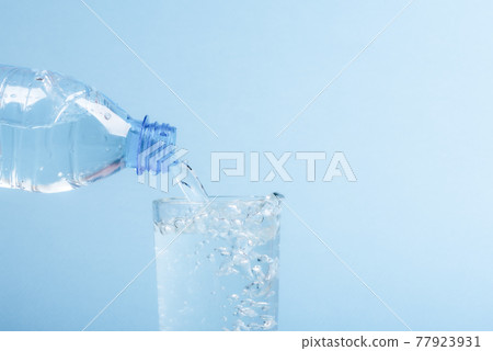 Pouring water from a plastic bottle into a glass beaker. 77923931