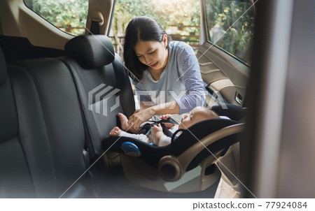 Asian young mother putting her baby son into car seat and fasten seat belts in the car 77924084