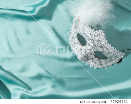 White venetian carnival mask with feather on green satin textile background 77924381
