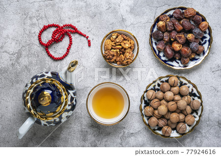 Popular food during Iftar - macadamia nuts, pistachios, walnuts, dry dates. Karan, rosary, teapot, bowl with black tea on concrete background Top view Flat lay Muslim holiday of holy month of Ramadan 77924616