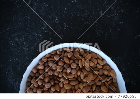 A wooden bowl with mixed nuts on top of a black concrete table. Healthy food and snacks. Nuts, pistachios, almonds, hazelnuts. A wooden bowl with mixed nuts on top of a black concrete table. Healthy food and snacks. Nuts, pistachios, almonds, hazelnuts. 77926553