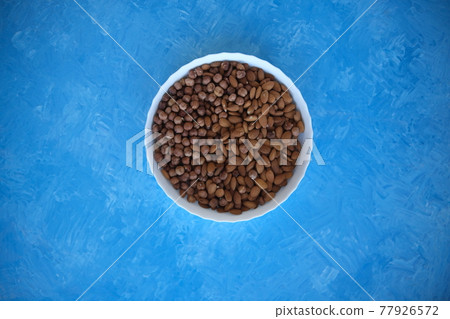 A wooden bowl with mixed nuts on top of a blue table. Healthy food and snacks. Nuts, pistachios, almonds, hazelnuts. A wooden bowl with mixed nuts on top of a blue table. Healthy food and snacks. Nuts, pistachios, almonds, hazelnuts. 77926572