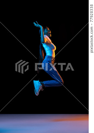 Young happy, joyful African girl jumping isolated over dark background in mixed neon light. Young happy, joyful African girl jumping isolated over dark background in mixed neon light. 77928338