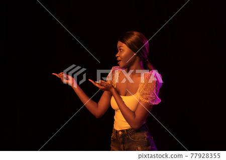 One young African beautiful girl isolated over dark background in mixed neon light. One young African beautiful girl isolated over dark background in mixed neon light. 77928355