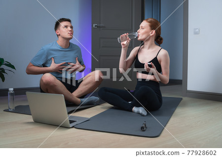During intense sports at home, a guy and a girl decided to take a break, drink water in front of a laptop 77928602
