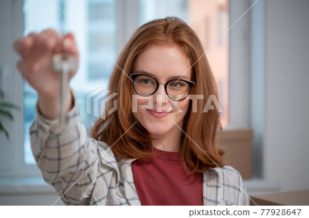 Portrait of a young girl with glasses, she shows the camera the keys to her new apartment 77928647