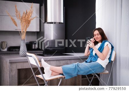 Woman bored and yawning watching media on mobile phone sitting on a chair at kitchen at home Woman bored and yawning watching media on mobile phone sitting on a chair at kitchen at home 77929550