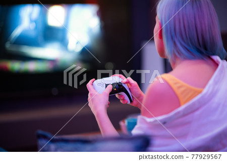 Teenager girl with colorful blue and pink hair hold joystick and play video games at home at night. 77929567
