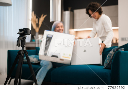 Happy videobloggers record unpacking video for their video blog with a brand new gaming console at home. 77929592