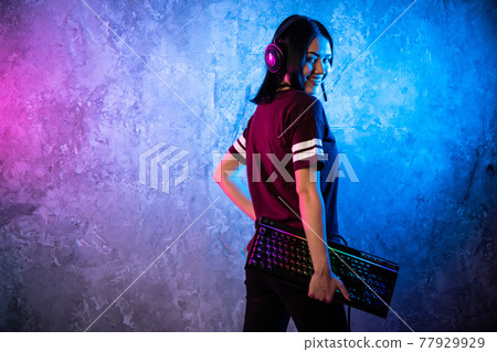 Female esports gamer posing with a gaming gear in neon light. Streamer girl standing with a gaming keyboard. Female esports gamer posing with a gaming gear in neon light. Streamer girl standing with a gaming keyboard. 77929929
