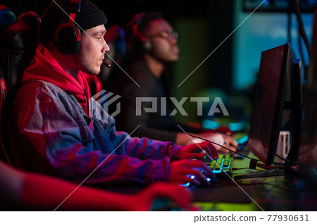 A multi-racial team of esports athletes conducts a training session before an online shooter tournament. Neon light. 77930631