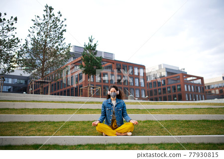 Woman with headphones doing yoga outdoors in park in city, coronavirus concept. 77930815