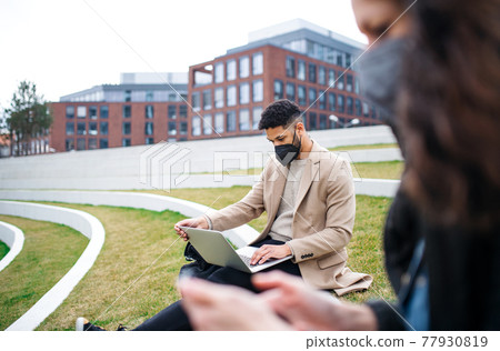 Man with laptop working outdoors in park in city, coronavirus concept. Man with laptop working outdoors in park in city, coronavirus concept. 77930819