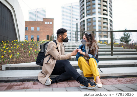 Man giving flower to woman outdoors in city, coronavirus, love and back to normal concept. Man giving flower to woman outdoors in city, coronavirus, love and back to normal concept. 77930820
