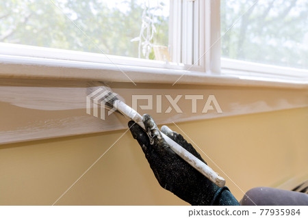 Hand of worker with gloves in the painting window molding trim Hand of worker with gloves in the painting window molding trim 77935984