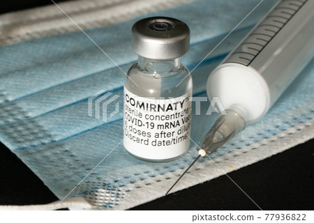 Den Helder, the Netherlands. May 2021. An ampoule of comirnaty vaccine, a mouth mask and a injection needle. 77936822