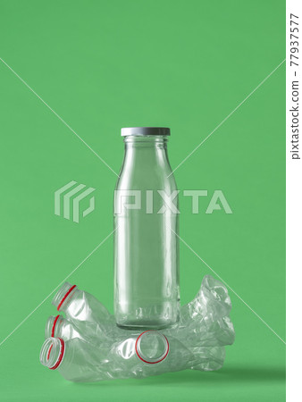 Glass over plastic bottles concept on a green background. 77937577