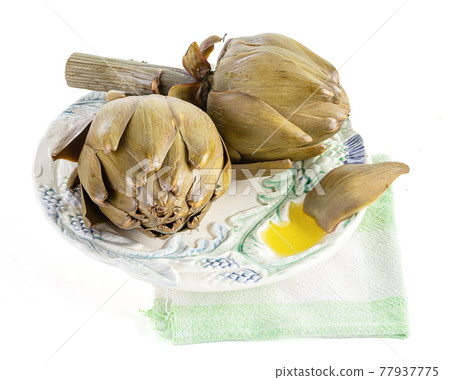 Two artichokes cooked in a plate with oil on a white background Two artichokes cooked in a plate with oil on a white background 77937775