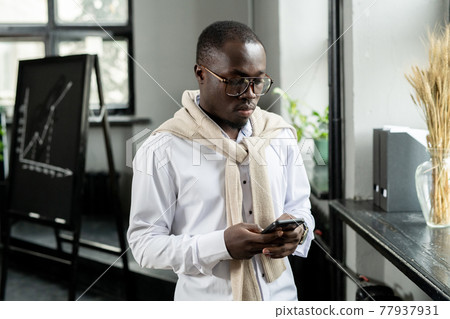 Young businessman of African ethnicity scrolling in smartphone 77937931
