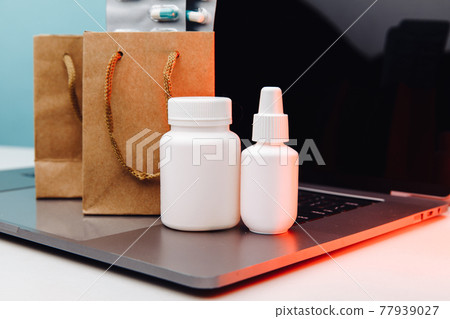 Online pharmacy. Paper bags with prescription drugs and pills and white conteiners on laptop Online pharmacy. Paper bags with prescription drugs and pills and white conteiners on laptop 77939027