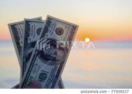 Three hundred dollar bills on background of sea surface at sunset dawn Three hundred dollar bills on background of sea surface at sunset dawn 77939227