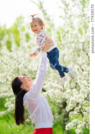 mom throws up her daughter in the park by a flowering tree. happy childhood. mom throws up her daughter in the park by a flowering tree. happy childhood. 77939570