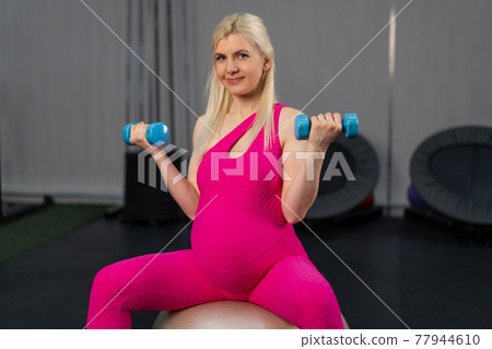 Pregnant woman exercise withdumbbells on fitness bal in gym 77944610