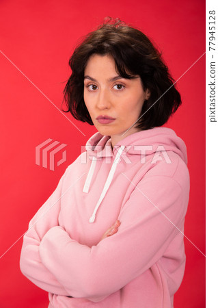Sexy woman with crossed arms seriously looks at camera on red background 77945128