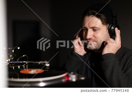 Young handsome millennial guy listens to music with headphones on dark bakdrop 77945148